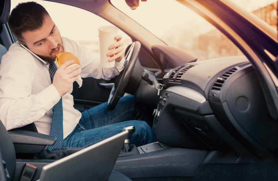 A distracted driver juggles eating, drinking, and talking on the phone.
